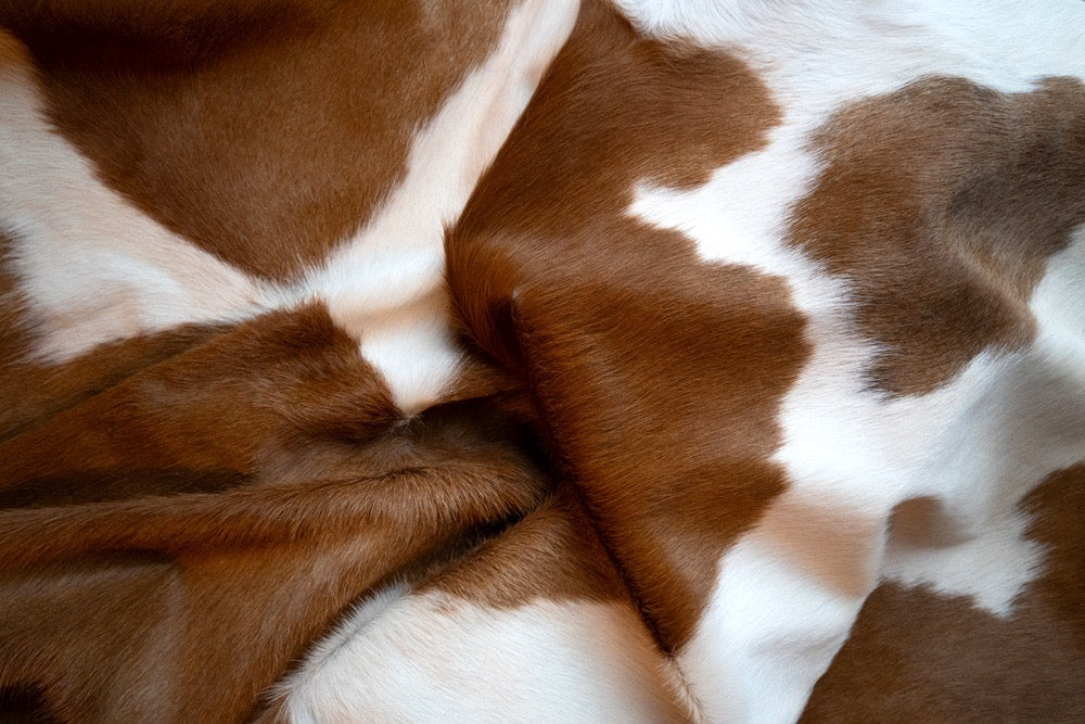 Brown and white cow print faux fur fabric with a soft, plush texture and natural drape.